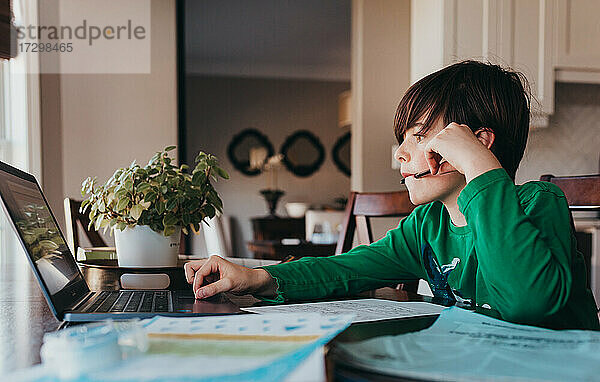 Junger Junge  der am Computer am Küchentisch online Schularbeiten erledigt.