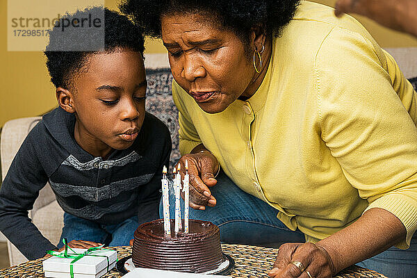 Großmutter und Enkel blasen zu Hause Kerzen auf dem Geburtstagskuchen aus