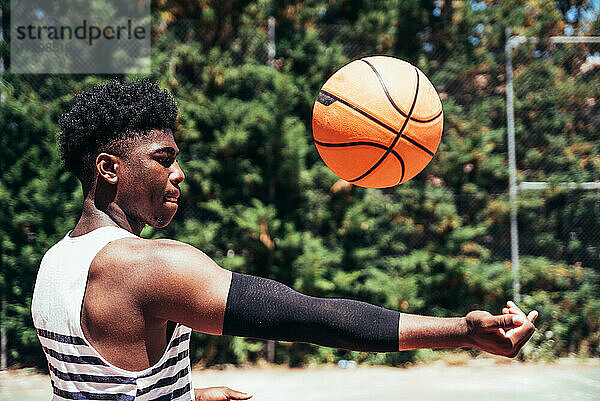 Seitenansicht eines schwarzen afroamerikanischen Jungen  der auf einem städtischen Platz mit einem Basketball spielt.