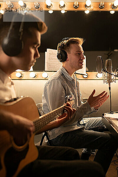 Männliche Musiker nehmen in einem professionellen Studio die Gesangs- und Gitarrenparts eines Songs auf