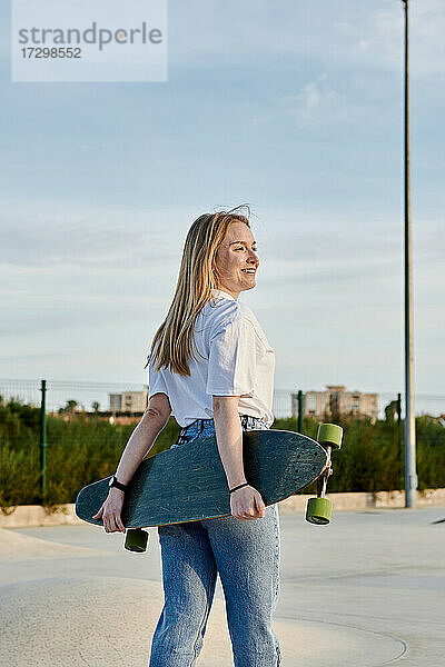 Junge blonde Frau lächelt und hat Spaß mit einem Skateboard