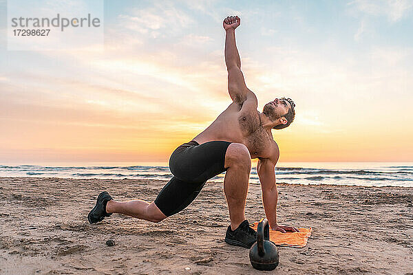 muskulöser Mann beim Training am Strand bei Sonnenaufgang