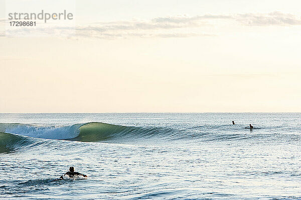 Freunde beim Surfen an einem glasklaren Tag bei Sonnenaufgang