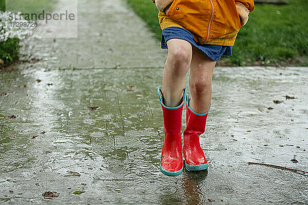 Nahaufnahme eines Kindes in bunten Regenstiefeln  das im Regen plantscht