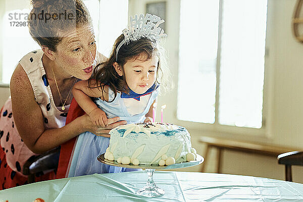 Mutter und Tochter blasen zu Hause Kerzen auf der Geburtstagstorte aus