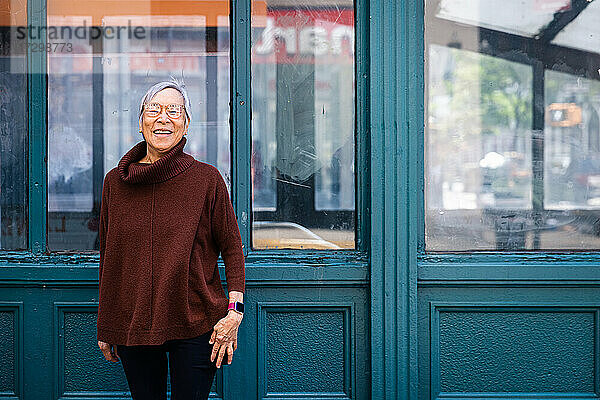 Glückliche ältere Frau lächelnd mit geschlossenen Augen stehend gegen die Stadtmauer