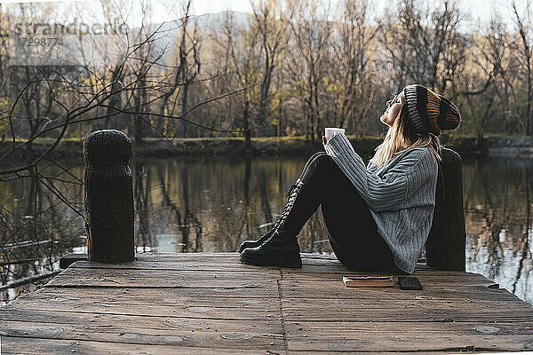 Frauen  die sich mit einer Tasse Kaffee auf einem Holzsteg am See entspannen.