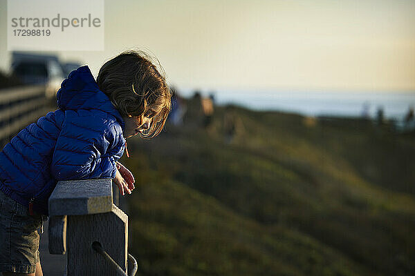 Seitenansicht eines Jungen  der sich während des Sonnenuntergangs am Geländer des Beobachtungspunkts anlehnt