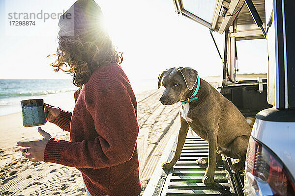 Frau und Hund am Morgen am Strand Auto-Camping