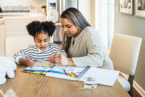 Mutter unterrichtet Tochter in Zeichnen auf Buch  während sie am Tisch sitzt