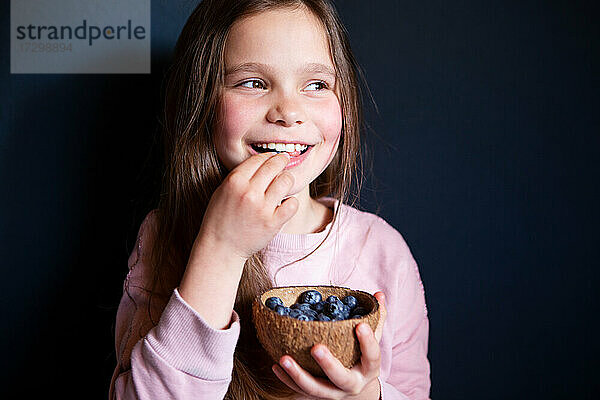 Lächelndes Mädchen pflückt frische Blaubeeren auf dunklem Hintergrund