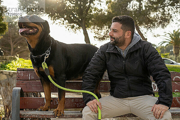 Mann sitzt auf einer Parkbank neben seinem Rottweiler-Hund