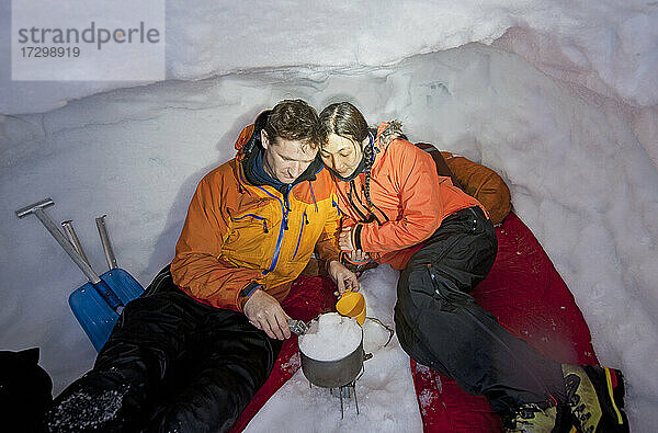 Paar schmilzt Schnee zum Kochen in einer Schneehütte in Island