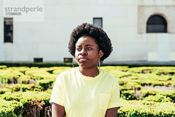 Porträt eines schwarzen Mädchens mit Afro-Haar und Ohrringen  das auf einer Bank in der Stadt sitzt.