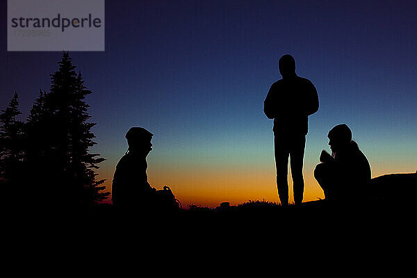 Eine Gruppe von drei Personen genießt einen Abend beim Zelten in den Bergen