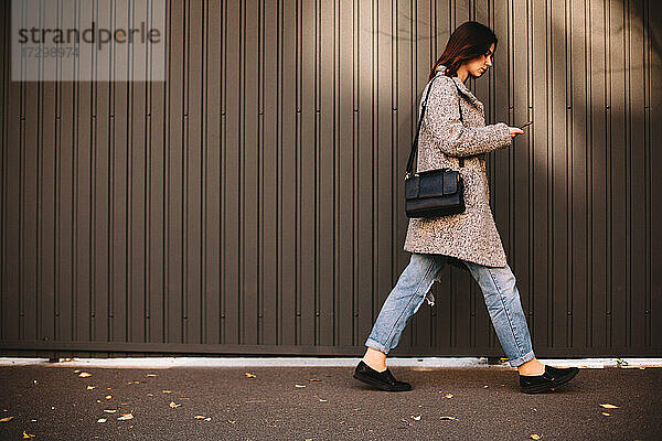 Seitenansicht einer nicht-binären Frau  die ein Smartphone benutzt und gegen eine Wand läuft