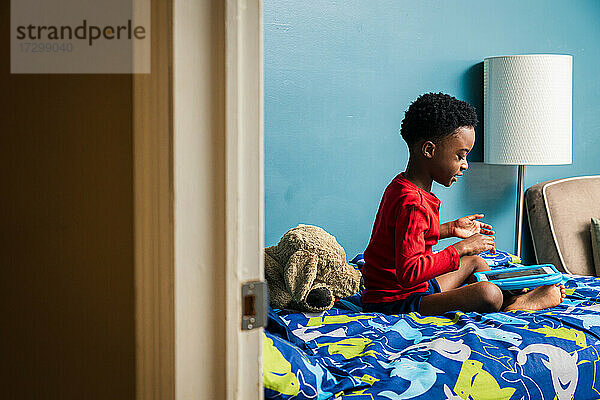 Junge gestikuliert bei der Verwendung eines digitalen Tablets im Schlafzimmer zu Hause