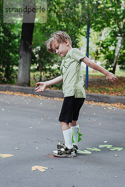 5 Jahre alt Junge Kind spielt im Freien  Kinder Outdoor-Aktivitäten  trägt grünes T-Shirt mit Dinosaurier-Druck und Dino-Helm