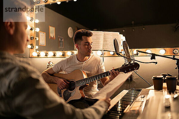 Erwachsener Mann spielt Musik auf der Gitarre  während er mit einem Freund im Studio Songs schreibt