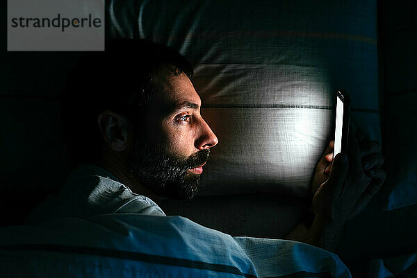 Junger Mann benutzt Smartphone im Bett