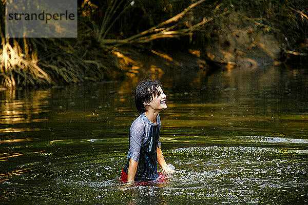 Ein glücklicher Junge spielt in einem Fluss im goldenen Sonnenlicht des Sommers