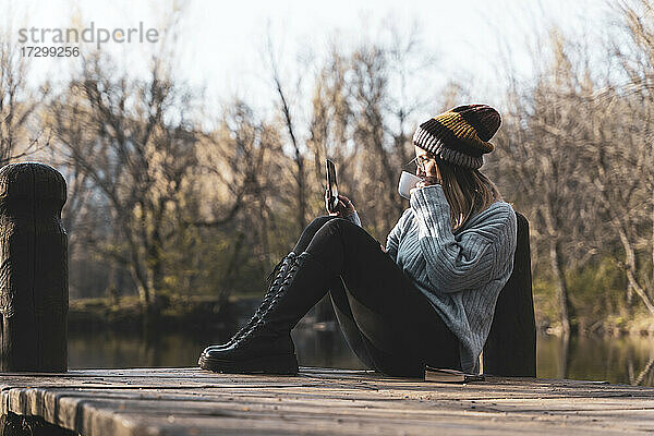 Frauen entspannen sich auf dem Holzsteg am See mit ihrem Smartphone.
