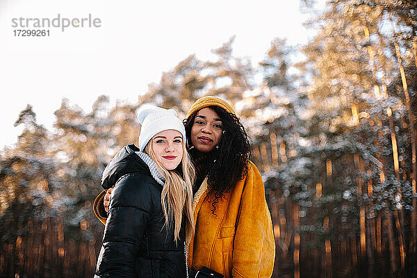 Porträt von zwei jungen Frauen  die im Winter an Bäumen stehen