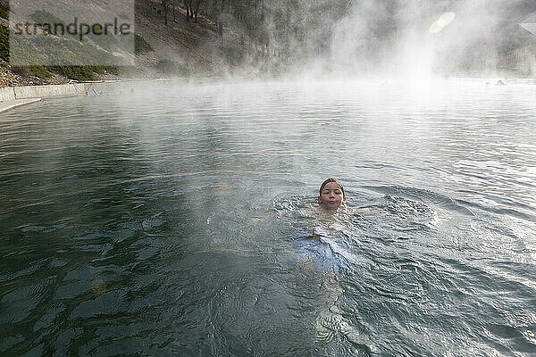 Ein Junge schwimmt in einem Pool von Trinity Hot Springs  aus dem Dampf aufsteigt