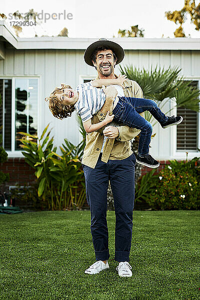 Verspielter Vater trägt glücklichen Sohn im Hinterhof stehend