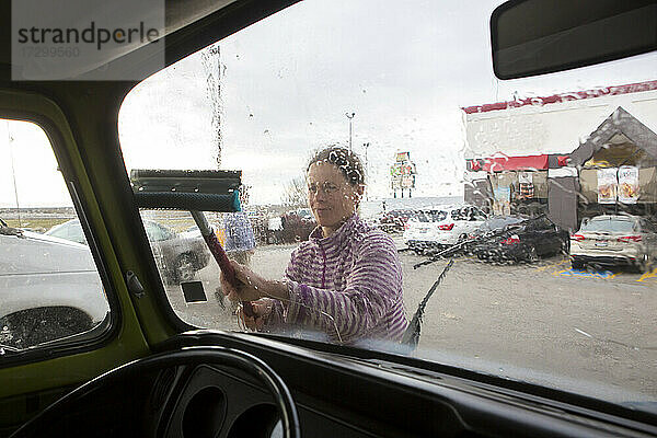 Eine Frau reinigt die Windschutzscheibe eines VW-Wohnmobils während eines Roadtrips