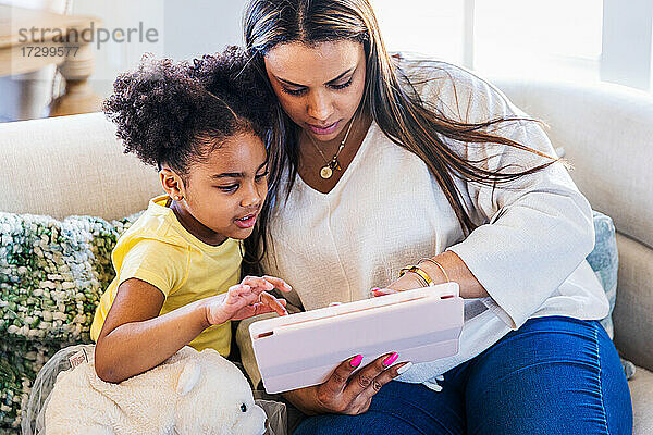 Mutter und Tochter benutzen ein digitales Tablet  während sie zu Hause auf dem Sofa sitzen