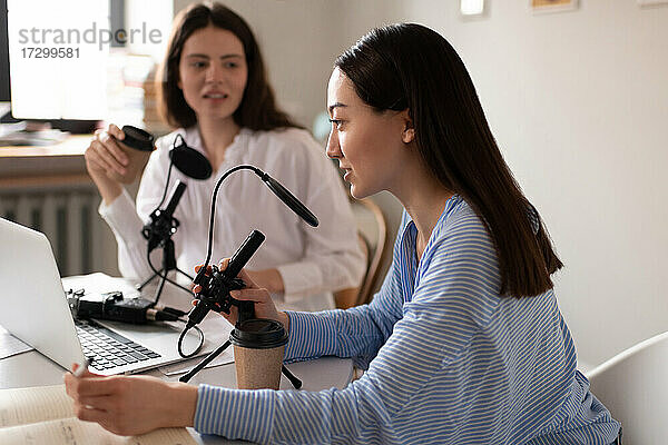 Asiatischer Blogger  der während eines Podcasts mit einem Freund im Studio ins Mikrofon spricht