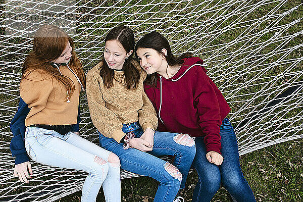 Drei junge Mädchen sitzen in einer Hängematte und unterhalten sich.