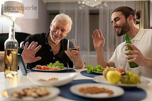 Junge und ältere Männer führen einen Videoanruf und essen zu Abend