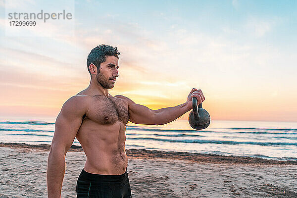muskulöser Mann beim funktionellen Training mit der Kettlebell am Strand von