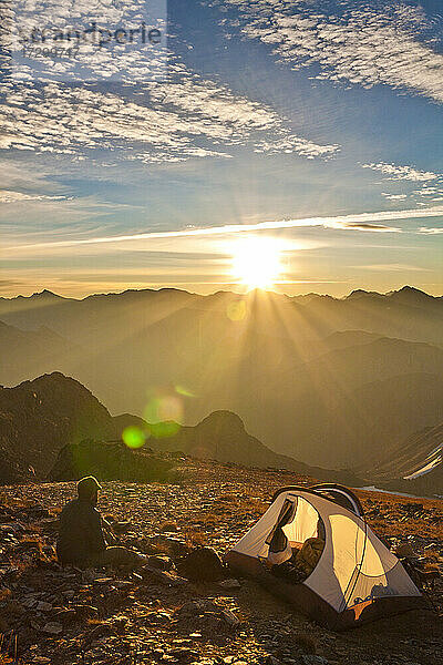 Ein Wanderer genießt den Sonnenaufgang von seinem Zeltplatz auf dem Gipfel eines Berges