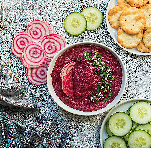 Schale mit Rüben-Hummus  Gemüse und Crackern auf grauem Hintergrund.