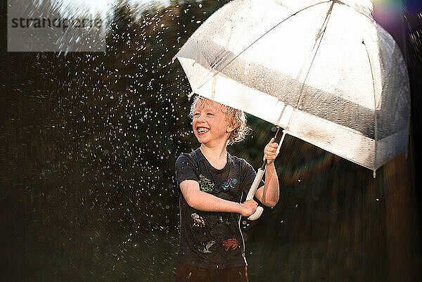 Glückliches Kind spielt im Regen unter Regenschirm