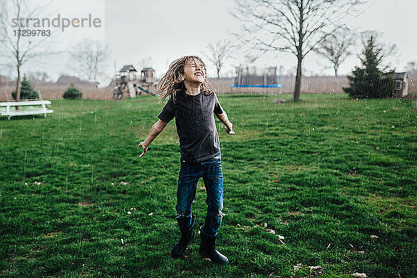 Kleiner Junge lachend und tanzend im Regen