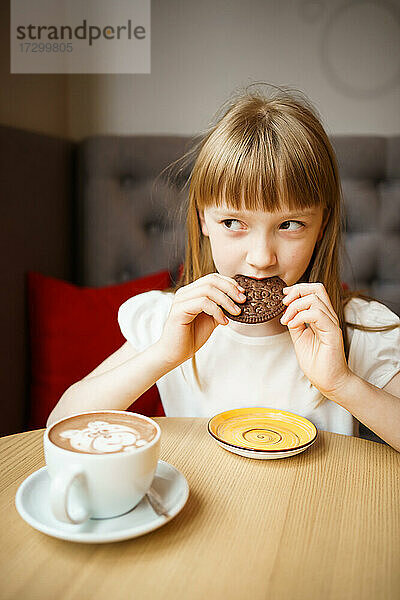 süßes Mädchen isst Schokoladenkekse und trinkt Kakao mit einem Muster