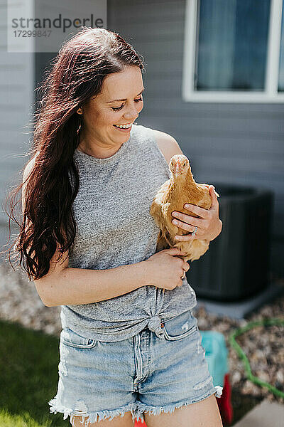 Frau hält Huhn in ihrem Garten an einem sonnigen Tag