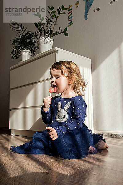 das Mädchen sitzt auf dem Boden und isst Süßigkeiten am Stiel