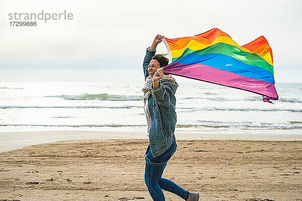 Frau lächelnd und läuft mit bunten LGBT-Flagge weht am Strand