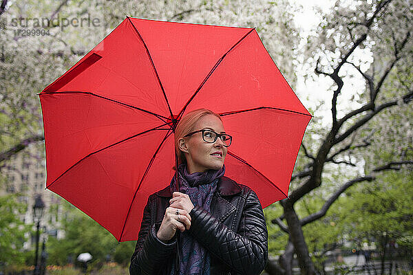 Frau mit leuchtend rotem Regenschirm im Frühlingspark