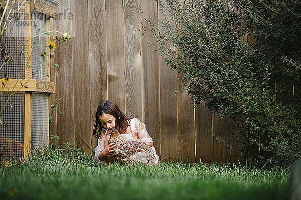 Ein süßes kleines Mädchen spielt mit einem Huhn in einem blumenübersäten Garten