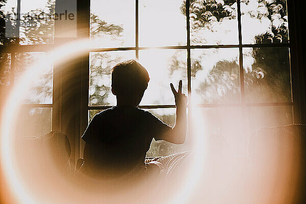 Back of Young Boy in Window Making Peace Sign With Circle Light Effect