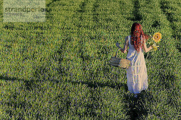 Weiß gekleidete Frau mit Weidenkorb und einer Sonnenblume im Gras