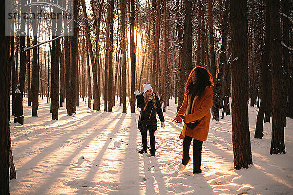 Glückliche Freundinnen spielen mit Schnee im Park im Winter