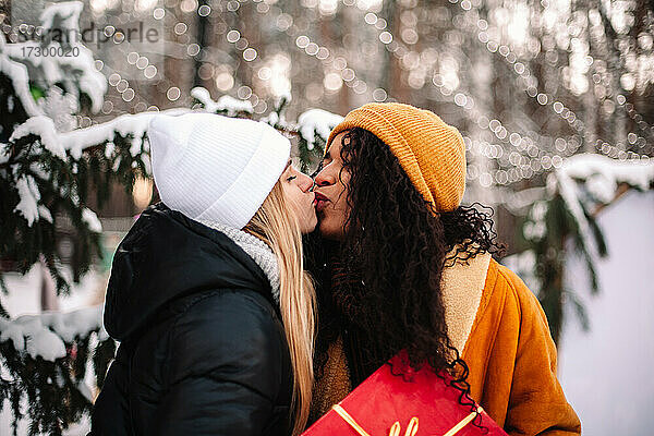 Glückliche Freundinnen  die sich küssen und ein Weihnachtsgeschenk unter dem Weihnachtsbaum halten