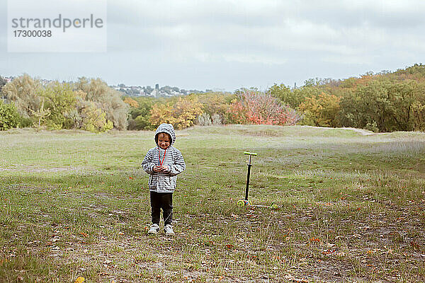 Kleine lächelnde Junge 4 Jahre alt Spaziergang mit Roller auf der grünen Wiese